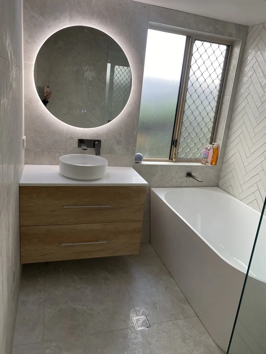 Bathroom with a round backlit mirror, timber vanity and bath