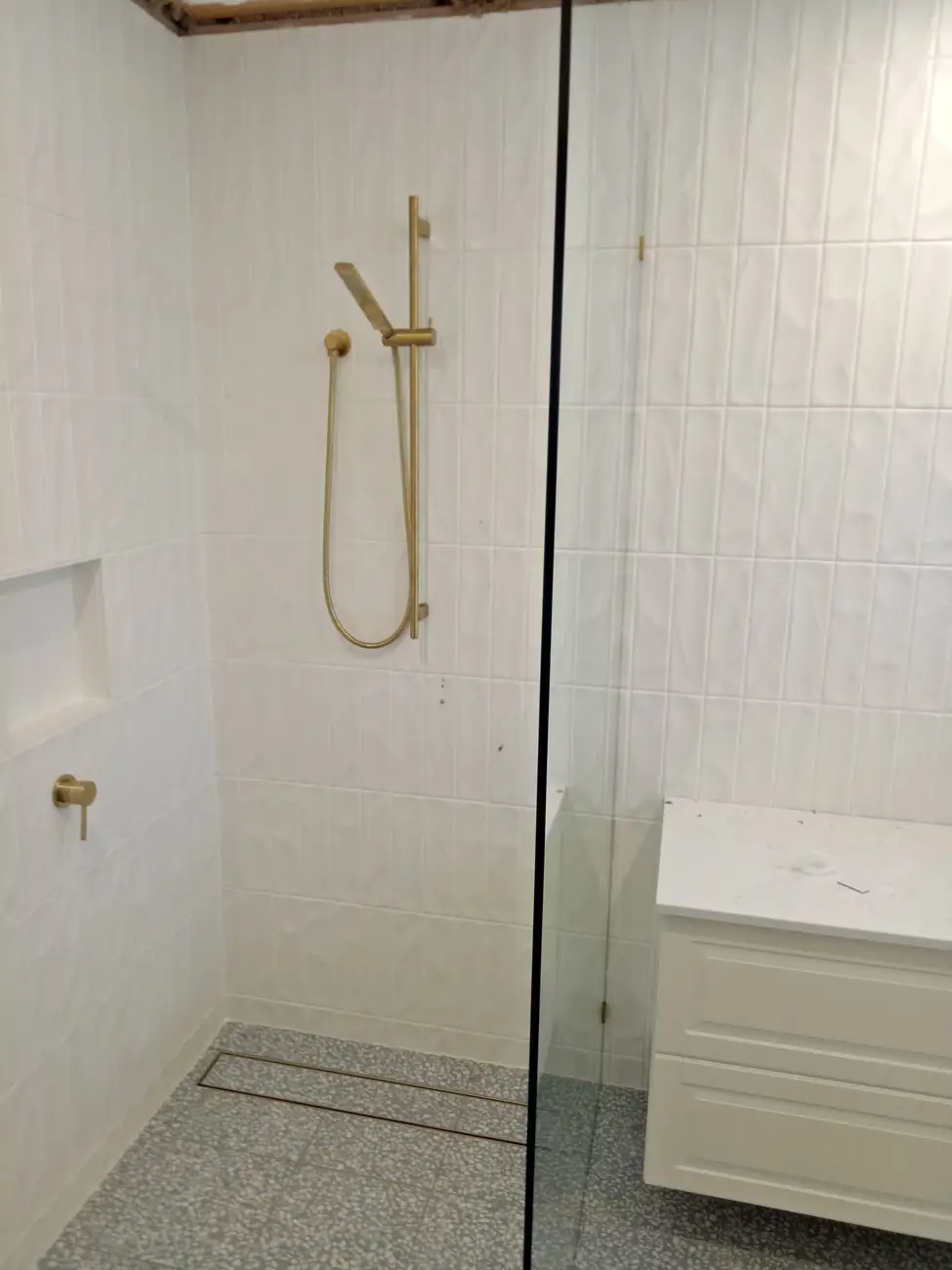 Shower in white vertical wall tiles with a brushed-brass rail, a niche and a linear drain