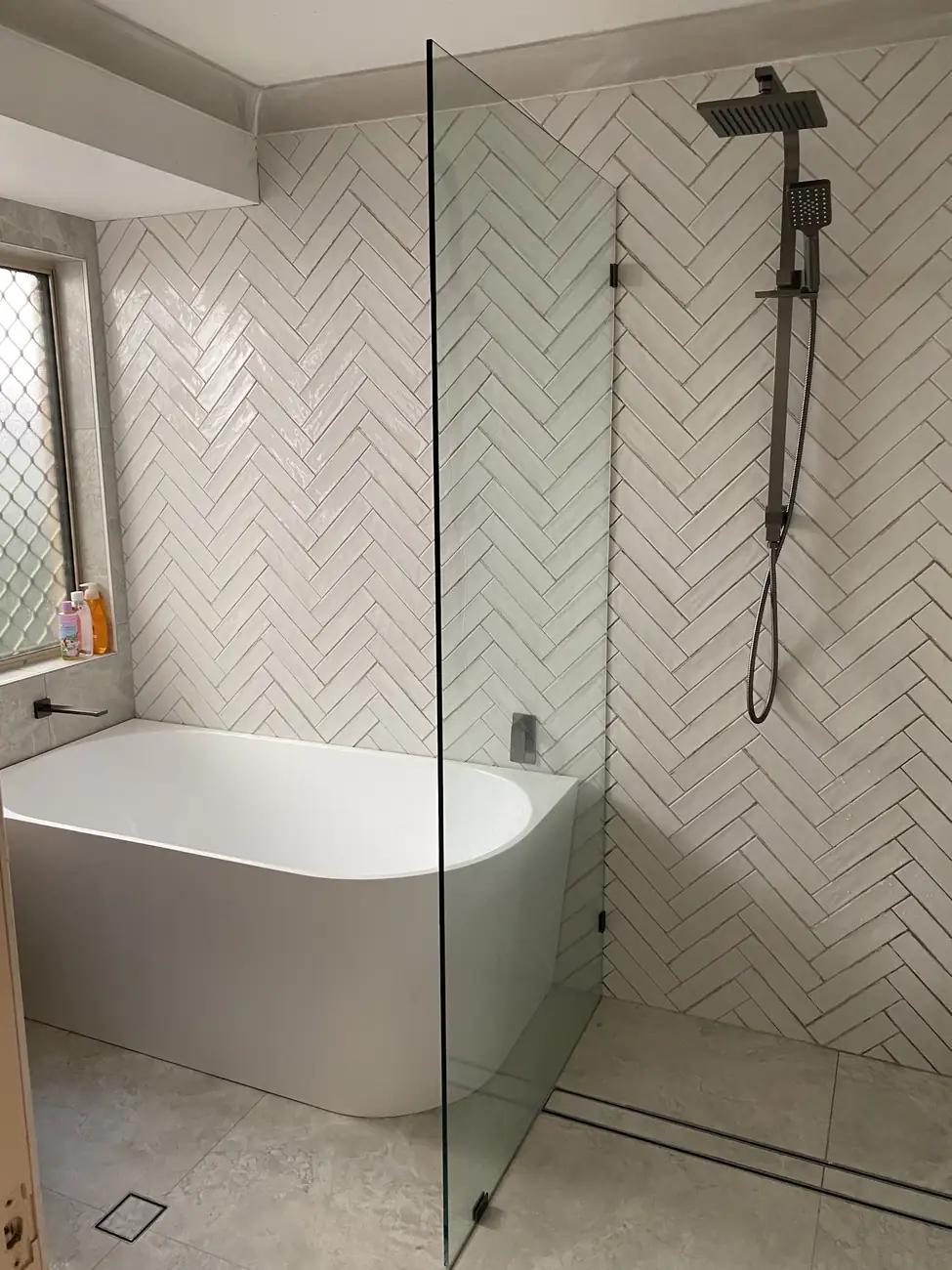 White herringbone wall tiles behind a freestanding bath and walk-in shower