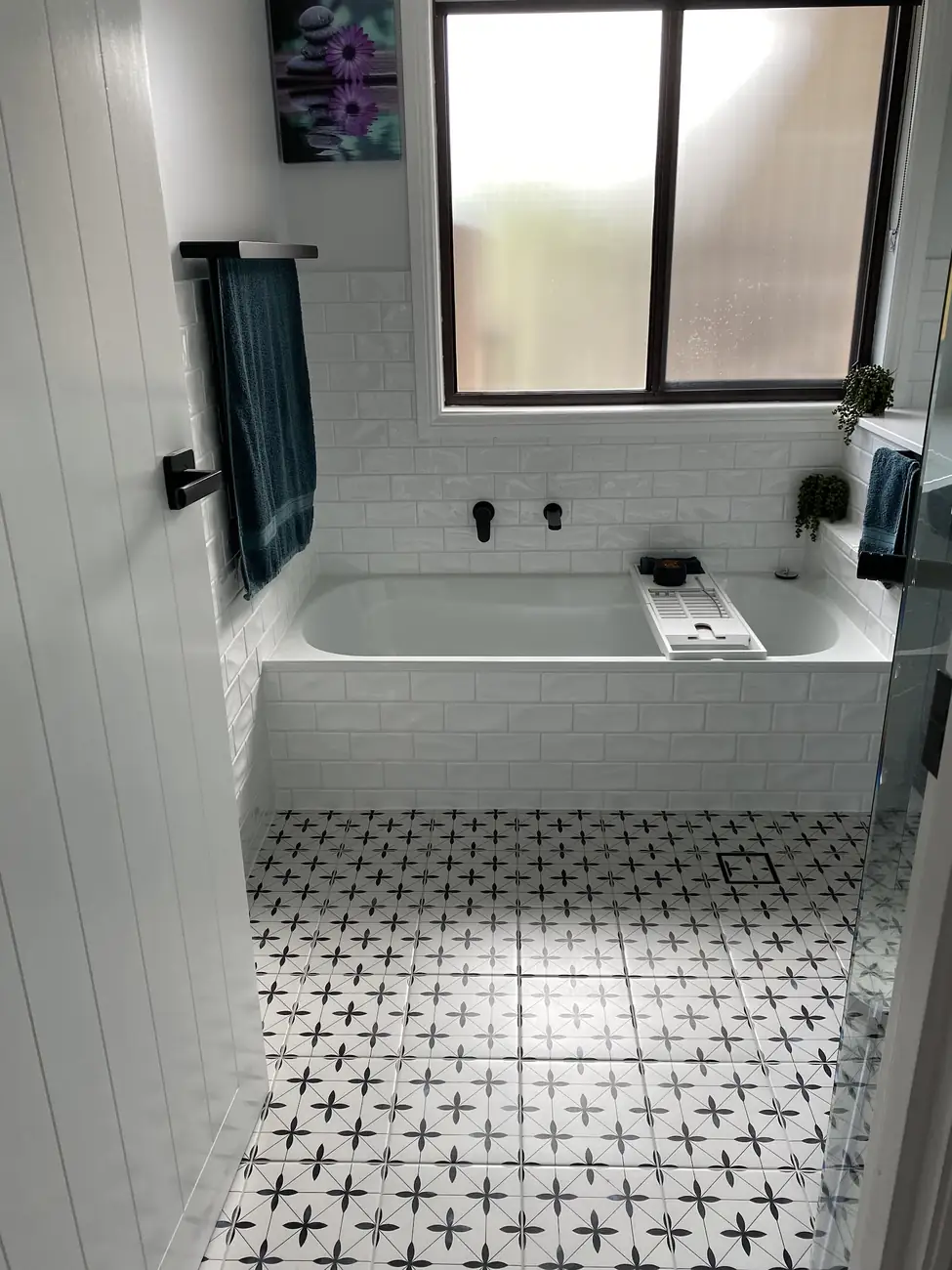 Bathroom with a black and white patterned floor, white subway-tiled bath surround and black tapware