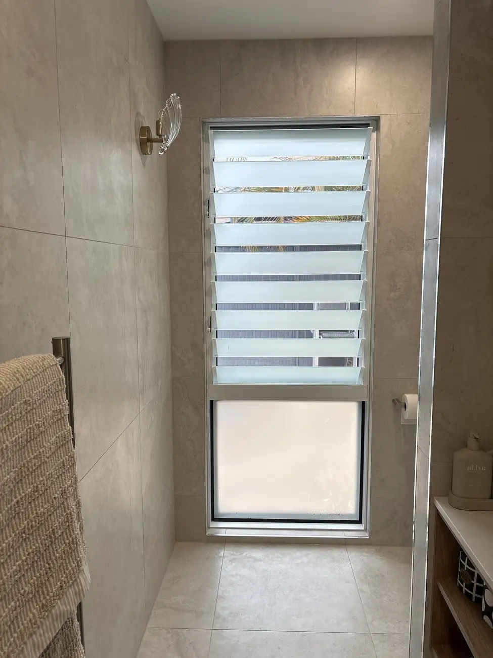 Shower tiled around a window, with light floor tiles and towel rail